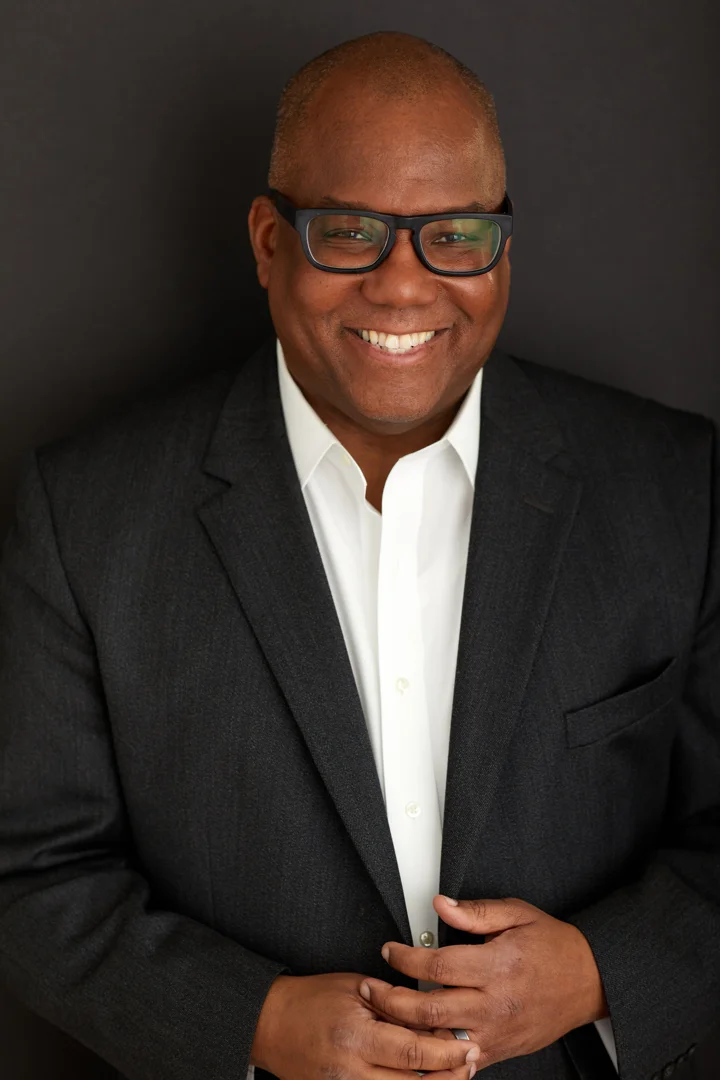 Kahlil Byrd standing in a charcoal suit and white shirt against a dark background
